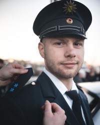 Polizeimeister Maximilian trägt seine ersten blauen Sterne auf der Schulter. Der junge Polizist trägt seine blaue Uniform und lächelt in die Kamera.
