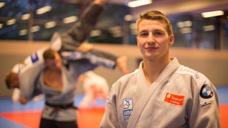 Judoka Hannes steht rechts im Bild. Hinter ihm zeigen gerade zwei Sportler eine Judo-Technik