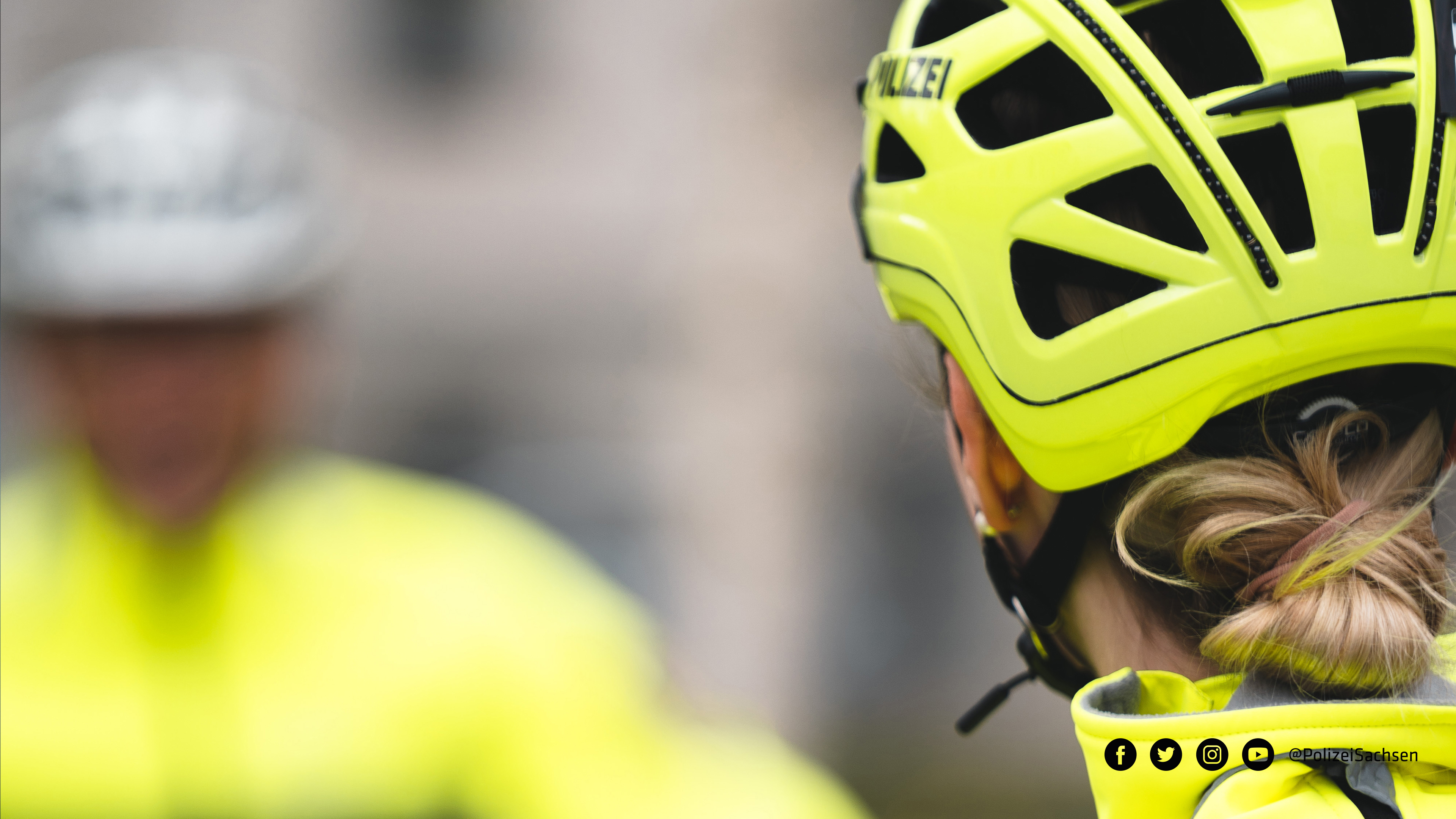 Eine Polizistin der Fahrradstaffel blickt zu ihrem Kollegen im Hintergrund. Zu erkennen sind die Teams an ihren auffälligen gelben Jacken und Helmen.