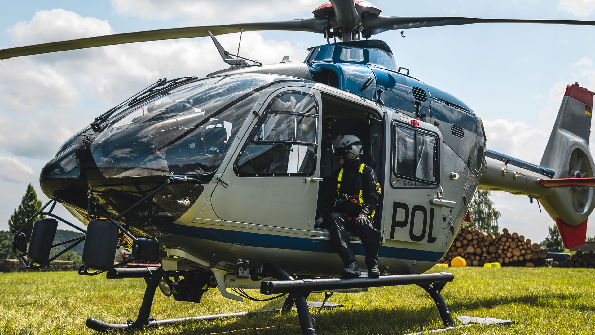 Der Polizei-Hubschrauber auf einer grünen Wiese kurz vor dem Start bei dem Übungseinsatz mit der Feuerwehr in Sebnitz. Eine Flugtechnikerin der Polizei sitzt in der geöffneten Tür des Helikopters und schaut in Richtung des Piloten.