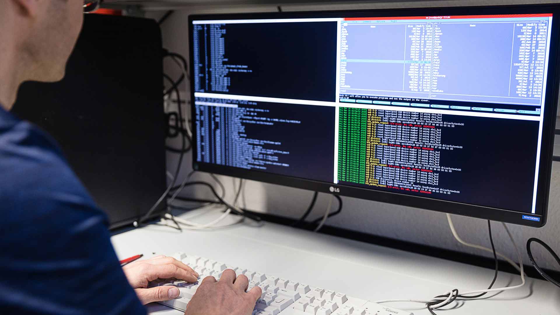 Ein Mann sitzt vor einem Computerbildschirm, auf dem mehrere Reihen mit Codes zu sehen sind.