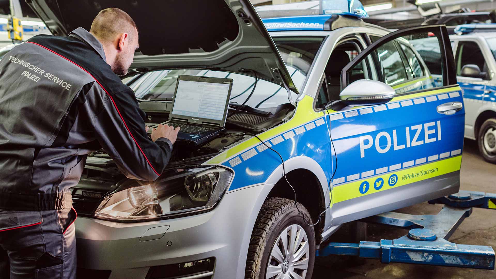 Ein Automechaniker steht an der geöffneten Motorhaube eines Streifenwagens der Polizei Sachsen.