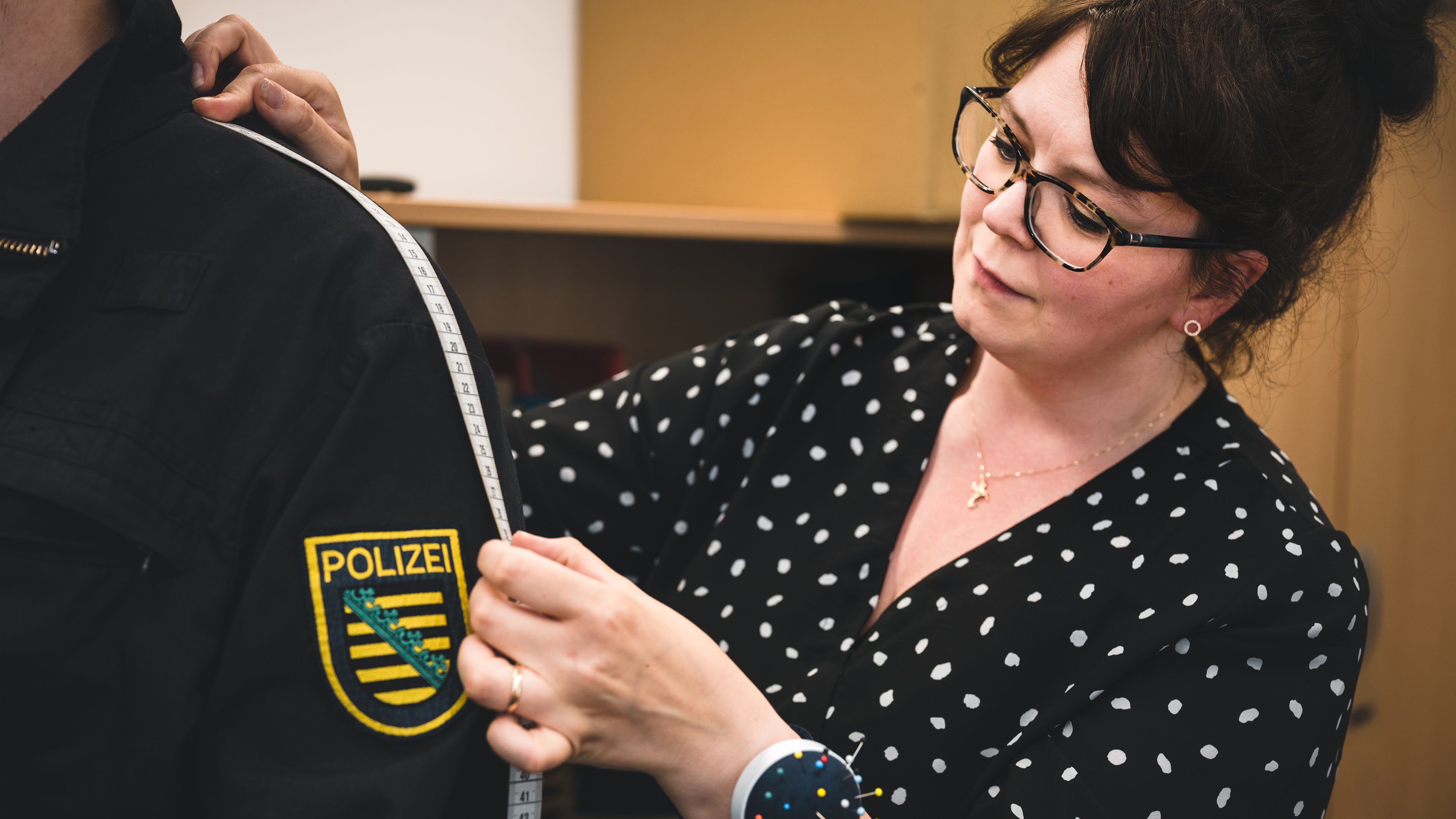 Eine Schneiderin des Polizeiverwaltungsamts bei ihrer Arbeit. Sie hält ein Maßband an eine Uniform.
