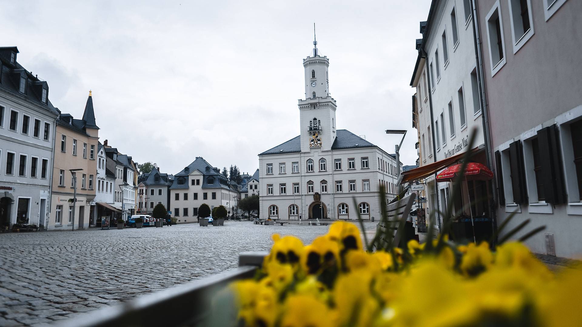 Das Foto zeigt den Marktplatz in Schneeberg. Links und recht befinden sich Gebäude mit Geschäften und Lokalitäten. Frontal ist das Rathaus zu sehen.